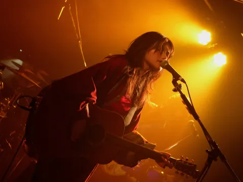 A singer playing guitar and singing into a microphone in an orange-lit venue with an energetic atmosphere.